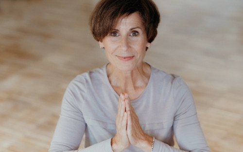 Birgit Brandes mit Händen in Gebetsstellung im Yoga lächelt in die Kamera